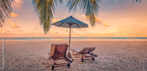 Beautiful tropical sunset scenery, couple chairs, loungers, umbrella under palm tree. Closeup sea sand sky horizon, colorful twilight clouds, relax tranquil vacation landscape. Summer holiday, idyllic