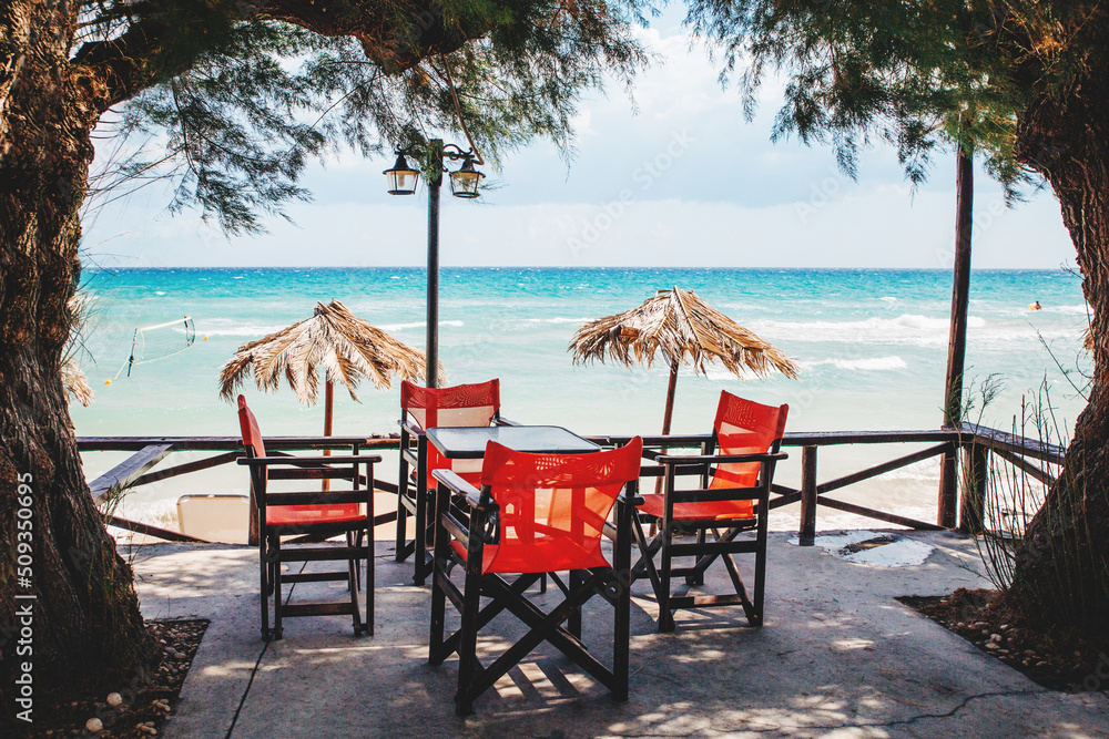 beautiful tropical beach with a frame of palm beach trees and blue sea ocean water. Travel destination scenic. Chill area with table and red chairs