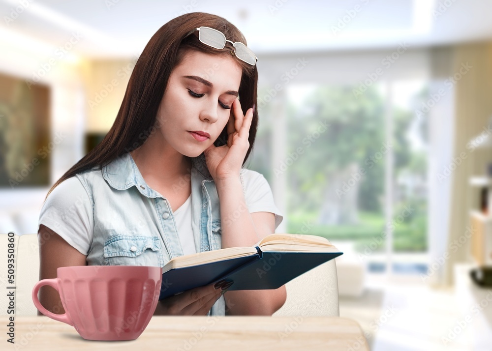 Fototapeta premium Young -woman drinking tea while reading book on sofa at home