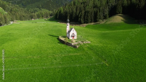 Val di Funes valley. green meadows and the baroque church of San Giovanni in Ranui. Drone footage with the transition to the mountains
 photo