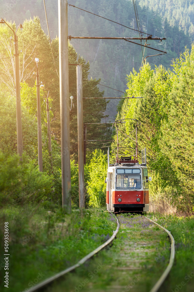 Fototapeta premium an old atmospheric tram in the forest against the background of mountains, an interesting colorful route train red wagon at the foot of the mountain in Russia Khakassia