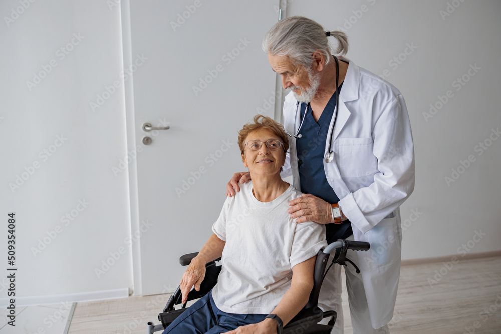 Professional male doctor carrying patient on wheelchair in medicine clinic. High quality photo Professional male doctor carrying patient on wheelchair in medicine clinic. High quality photo