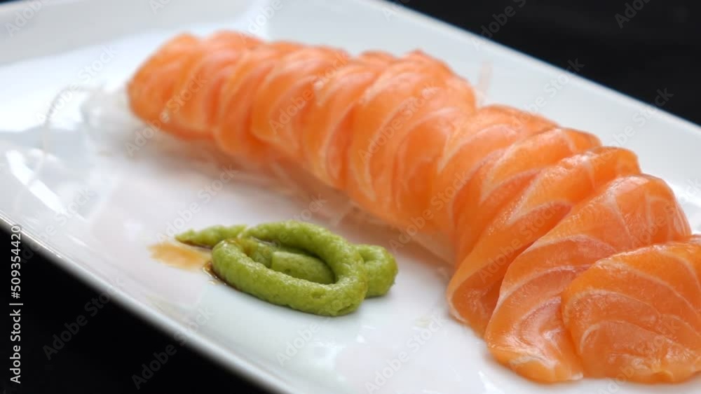 Close up hand using chopsticks to pick up salmon slow motion