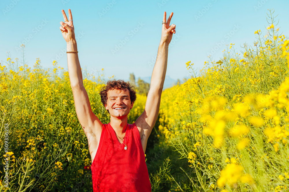Portrait of young cheerful homosexual man doing peace sign with hands at rapeseed field at spring. Portrait of young cheerful homosexual man doing peace sign with hands at rapeseed field at spring.