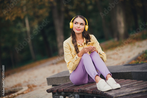 Portrait of beautiful trendy dreamy girl sitting on bench listening pop hit different melody enjoying resting outdoors