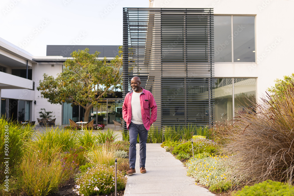Full length of bald african american senior man with hands in pockets looking at plants in yard Full length of bald african american senior man with hands in pockets looking at plants in yard