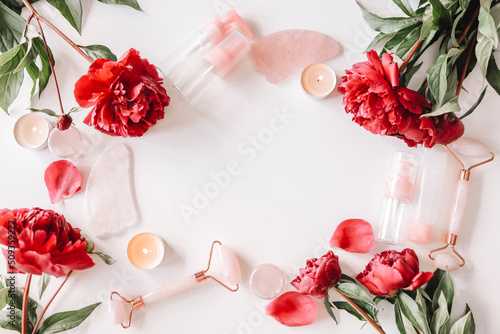 Cosmetic products bottles, face roller and gua sha massager, pink peonies flowers on white background. Banner. Top view. Spa relax, body treatment, spa, skin care concept