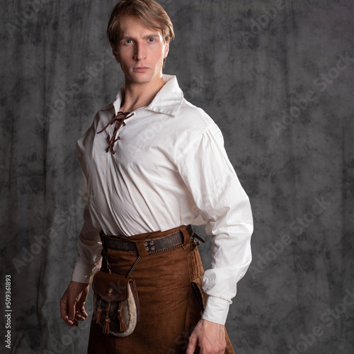 A young man in a leather kilt and a white lace-up blouse. A Scottish, Photo in the studio on a gray background