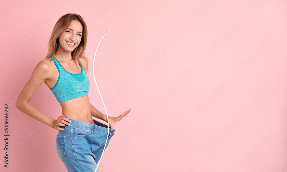 Happy young woman with slim body in oversized jeans on pink background, space for text. Weight loss - obrazy, fototapety, plakaty 
