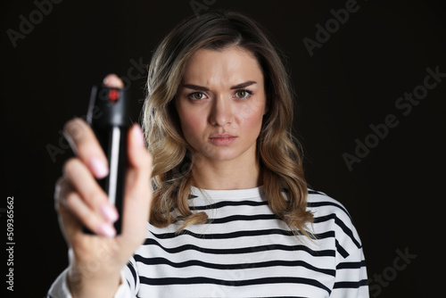 Young woman using pepper spray on black background