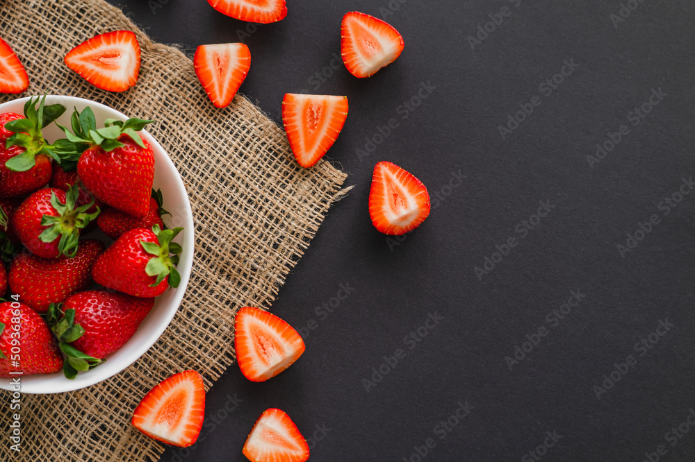 Top view of juicy strawberries in bowl on sackcloth on black background. Top view of juicy strawberries in bowl on sackcloth on black background.