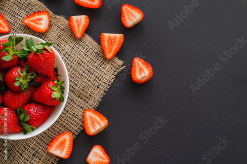 Top view of juicy strawberries in bowl on sackcloth on black background.