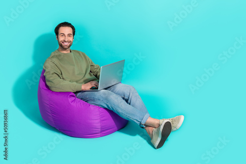 Full size profile side photo of young guy purple beanbag use laptop manager isolated over turquoise color background
