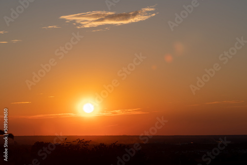 A wonderful sunset with a few fluffy clouds  covering the rolling hills of south Limburg in the Netherlands with an orange and golden glow  creating a magical atmosphere over the agricultural fields.