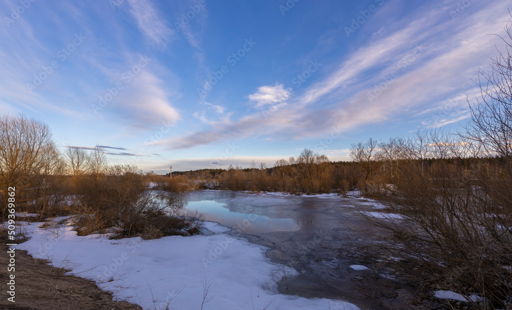 Cold spring evening. Ice and snow melt on the river. Clouds in the evening sky. Colorful landscape.