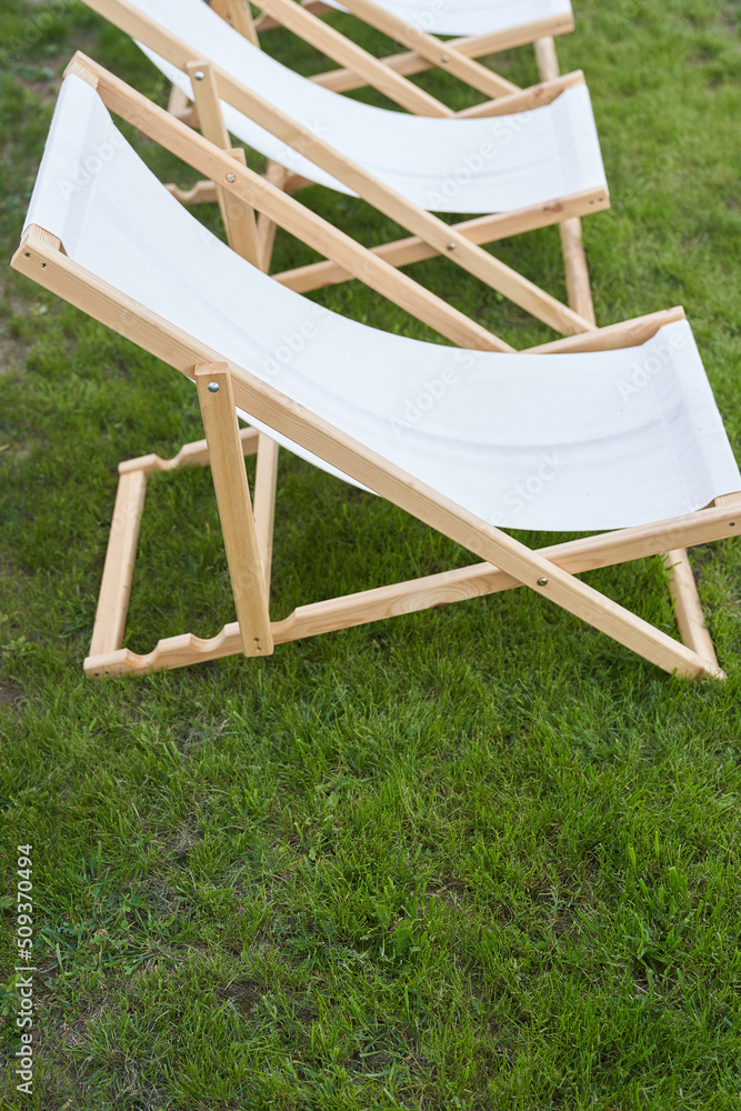 Three white wooden sun beds on the lawn, the backyard of a country house, a recreation concept. Copy space. High quality photo Three white wooden sun beds on the lawn, the backyard of a country house, a recreation concept. Copy space. High quality photo