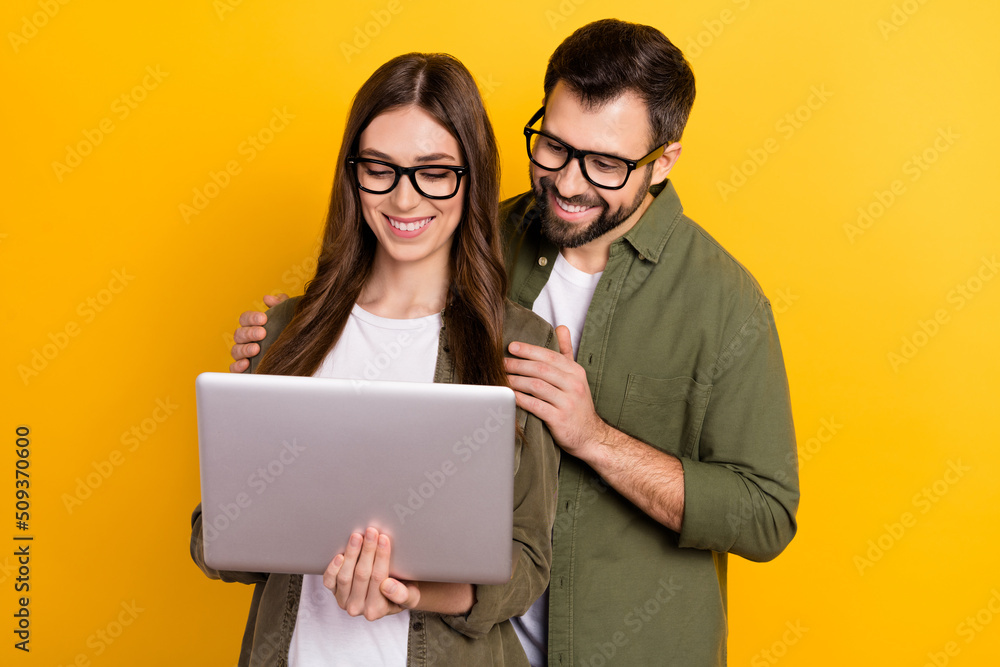 Photo of cute intelligent couple surfing in internet choose clothes buy stuff isolated on yellow color background Photo of cute intelligent couple surfing in internet choose clothes buy stuff isolated on yellow color background