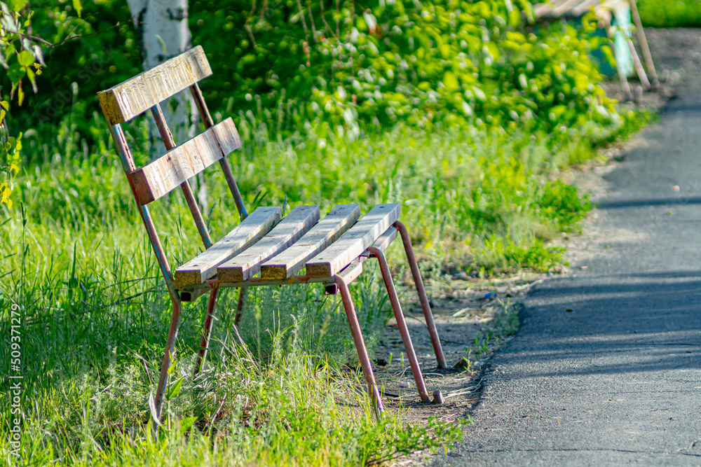 A wooden bench standing on the street of a provincial town surrounded by green vegetation. Close-up. Soft focus A wooden bench standing on the street of a provincial town surrounded by green vegetation. Close-up. Soft focus