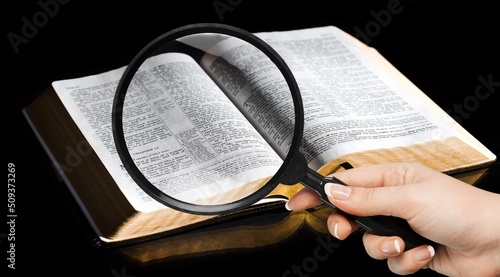 A magnifying glass in hand with open bible book. photo