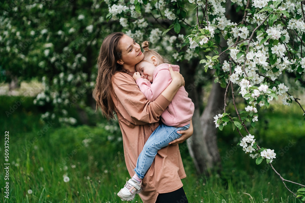 young mother with her daughter in her arms in a blooming apple orchard young mother with her daughter in her arms in a blooming apple orchard