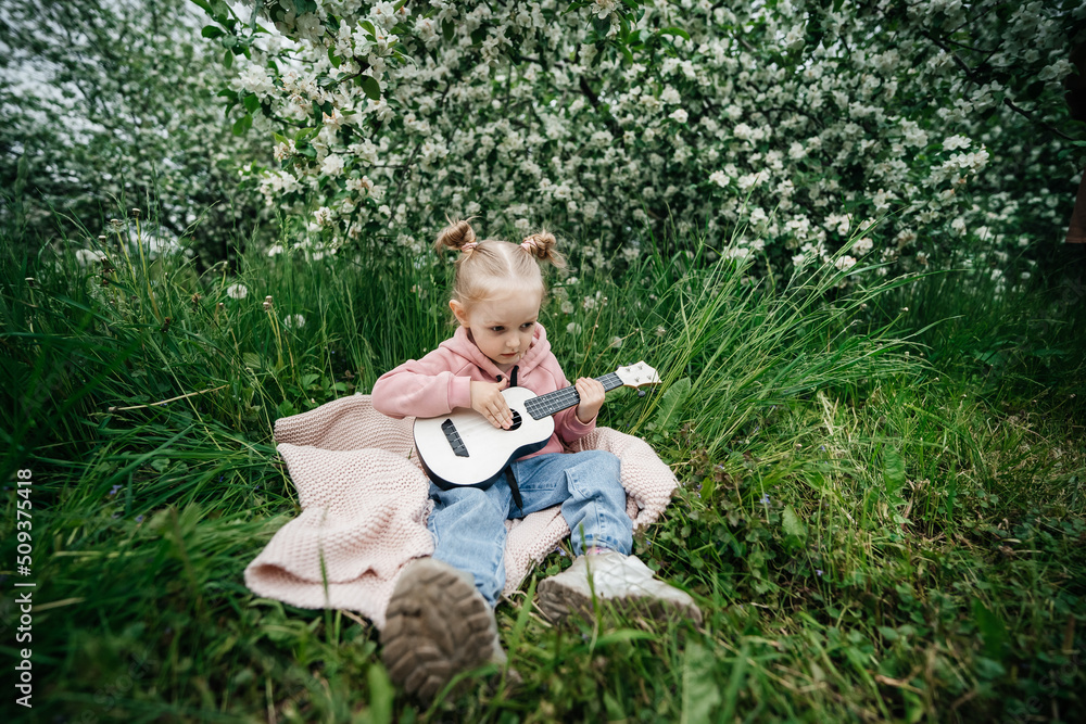 little girl playing the ukulele in a blooming apple orchard in nature little girl playing the ukulele in a blooming apple orchard in nature