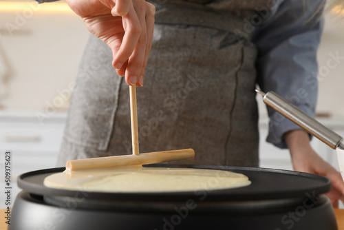 Woman cooking delicious crepe on electrical pancake maker in kitchen, closeup