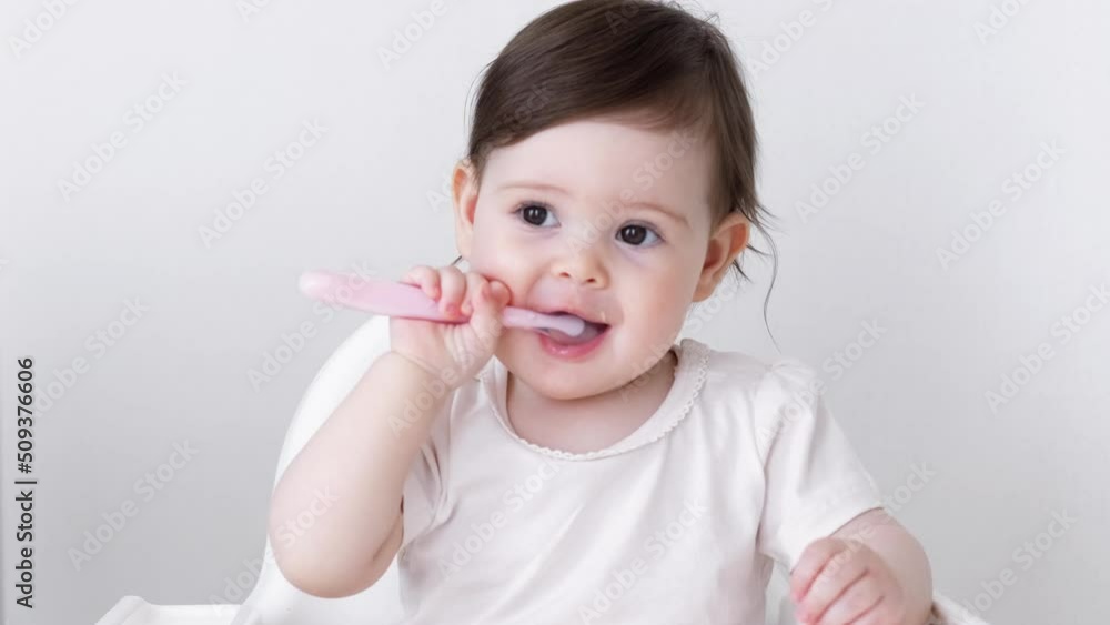 Baby girl eating blend mashed food sitting, on high chair, mother feeding child, hand with spoon for vegetable lunch, baby weaning, first solid food for young kid. Baby girl eating blend mashed food sitting, on high chair, mother feeding child, hand with spoon for vegetable lunch, baby weaning, first solid food for young kid.