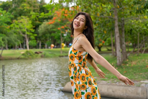 Portrait photo of a young beautiful asian female lady in sunflower summer pattern dress embracing the breeze wind relaxingly and chillingly in a public park photo