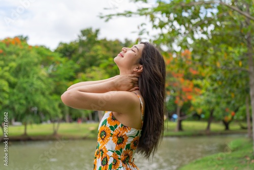 Portrait photo of a young beautiful asian female lady in sunflower summer pattern dress embracing the breeze wind relaxingly and chillingly in a public park photo