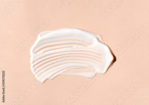 Texture of white cream on beige background. Smear of moisturizer closeup. Lotion swatch. Beauty, skin care product smear smudge drop. SPF sunscreen cream sample