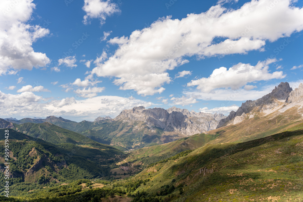 general view of a valley with the Picos de Europa and the cloudy blue sky in the background