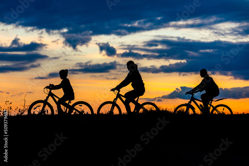 family cyclist and bicycle silhouettes on the dark background of sunsets. mom and her children ride bicycles against the backdrop of sunset.
