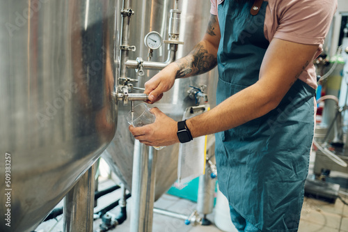 Close shot of a man filling glass of beer on a tap in brewery