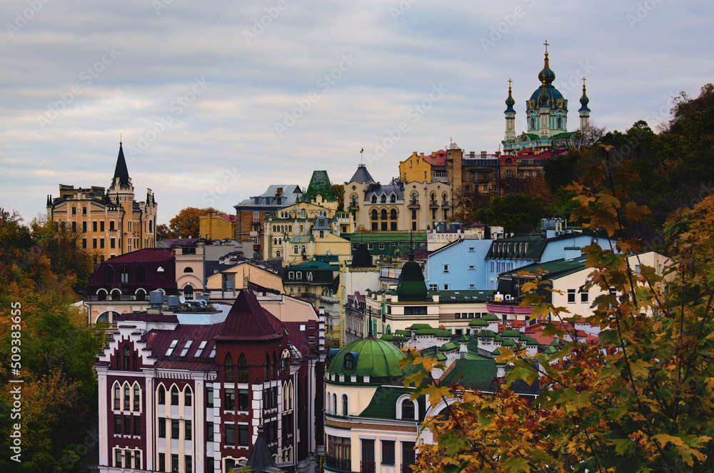 Naklejka premium Picturesque autumn landscape of colored roofs of Andrew's Descent (Andriyivsky uzviz, Podil neighborhood). Famous Saint Andrew's Church and house number 15th, called The Richard's Castle-Lion Heart
