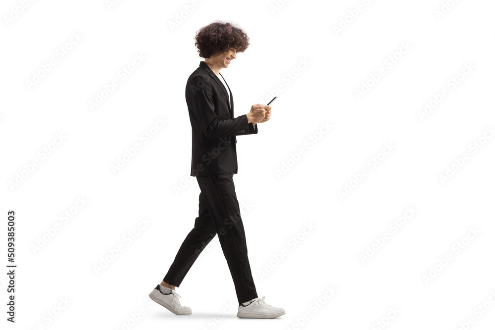 Obraz premium Full length profile shot of a young tall man walking and using a smrtphone
