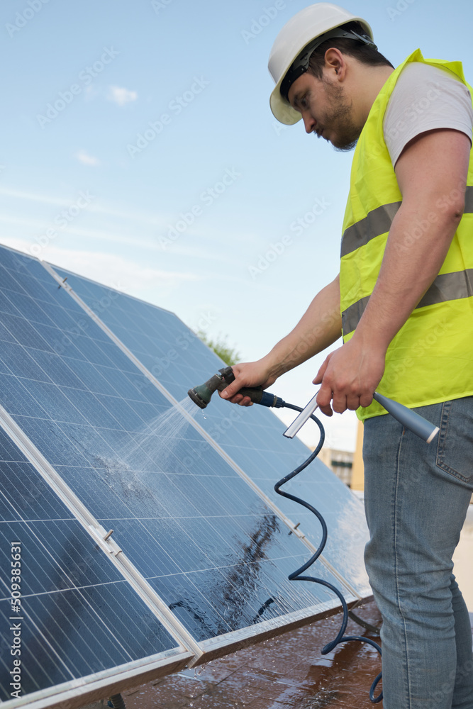 Technician washing solar panels with a hose. Technician washing solar panels with a hose.