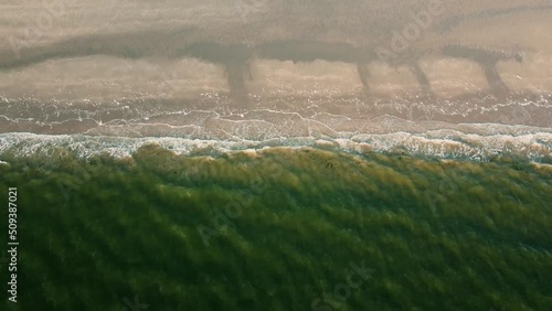 Droneshot of a shore from above with green water splashing onto the beach