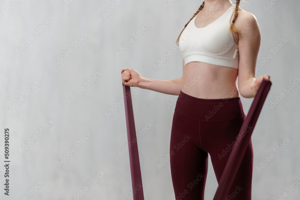 Close-up of sports woman in fashion sportswear exercising with elastic band stretch over greay background. Close-up of sports woman in fashion sportswear exercising with elastic band stretch over greay background.