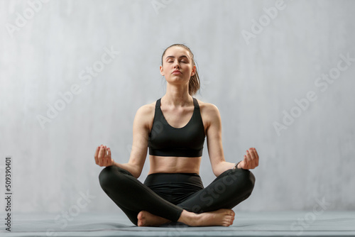 Young healthy woman in black sportsclothes practising yoga in studio, in a yoga position, copy space