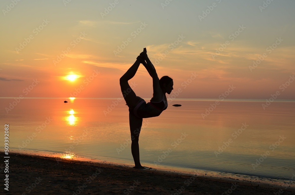 Silhouette shaped woman doing exercises and yoga moves at sunset on a beach.