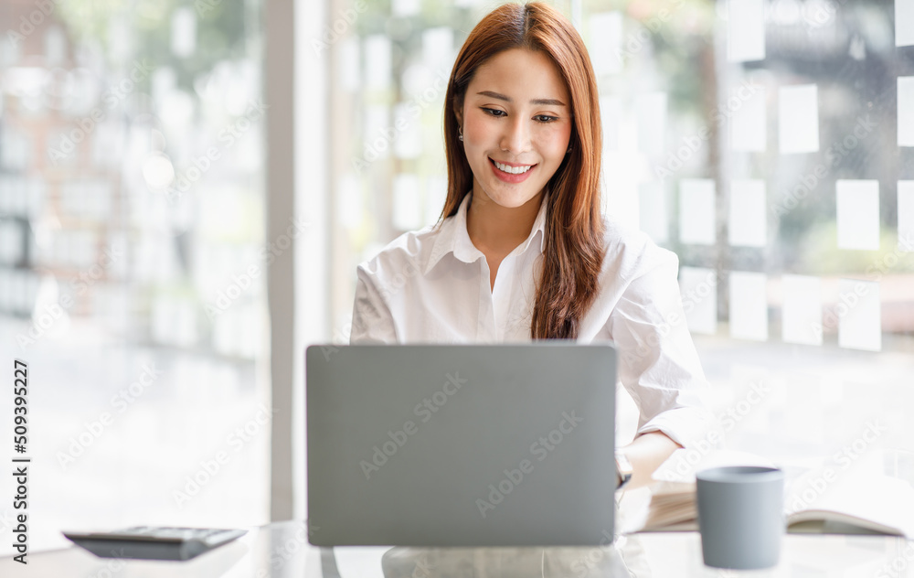 Portrait of happy Asian businesswoman using laptop computer while working with using a calculator to calculate the numbers, finance accounting concept Portrait of happy Asian businesswoman using laptop computer while working with using a calculator to calculate the numbers, finance accounting concept