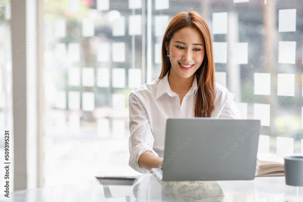 Portrait of happy Asian businesswoman using laptop computer while working with using a calculator to calculate the numbers, finance accounting concept Portrait of happy Asian businesswoman using laptop computer while working with using a calculator to calculate the numbers, finance accounting concept