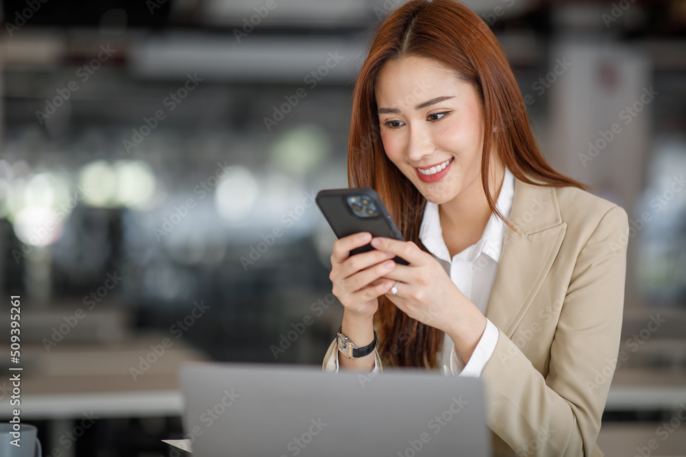 Photo of the adorable young lady working on laptop computer and holding smartphone at office indoors, Asian business woman. Photo of the adorable young lady working on laptop computer and holding smartphone at office indoors, Asian business woman.