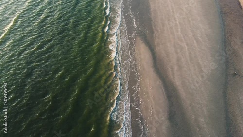 Droneshot of a shore from above with green water splashing onto the beach
