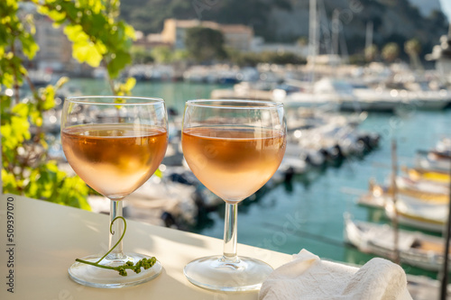 Cold rose wine in glasses served on outdoor terrace in sunlights with view on old fisherman's harbour with colourful boats in Cassis, Provence, France