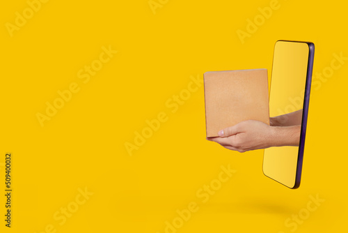 Male hands holding out parcel from modern smartphone on yellow background. Online shopping, service and delivery concept. photo