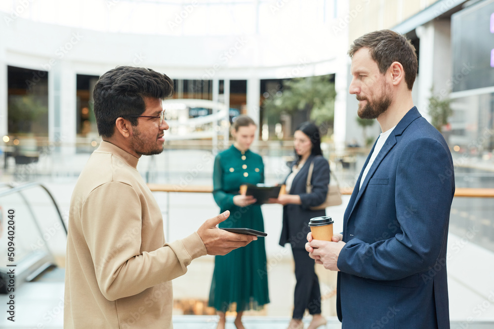 Side view portrait of two businessmen talking while standing in office building setting