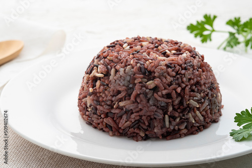 Cooked brown rice or riceberry rice on white plate on wood table