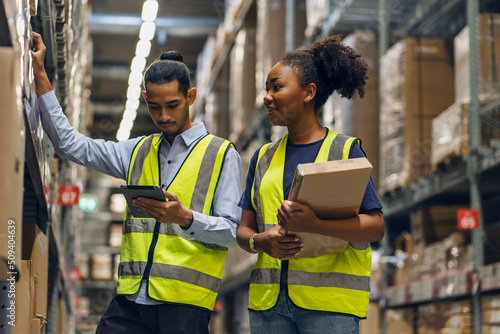 Фотография female African American employee and an Asian employee wearing a uniform holding tablet and working together to inspect goods in the warehouse