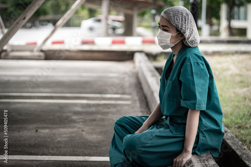Tired depressed female asian scrub nurse wears face mask blue uniform sits on hospital floor,Young woman doctor stressed from hard work